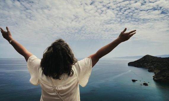 Woman with arms outstretched overlooking the ocean.